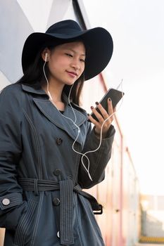 vertical photo of a happy young asian woman with earphones making a video call with her smart phone, concept of technology and modern lifestyle