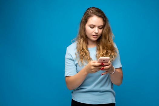 Portrait of a happy woman holding smartphone and texting a message or chatting with a friend via messenger over blue background