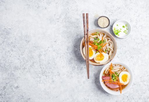 Bowls with Japanese soup ramen, chopsticks, white concrete rustic background. Traditional Asian soup with noodles, meat, eggs. Asian food. Japanese ramen for dinner. Space for text. Ramen, top view