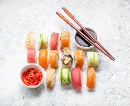 Assorted sushi set on white concrete background. Japanese sushi, rolls, soy sauce, ginger, chopsticks. Top view. Sushi nigiri. Japanese dinner/lunch. Different sushi mixed. Japanese food concept