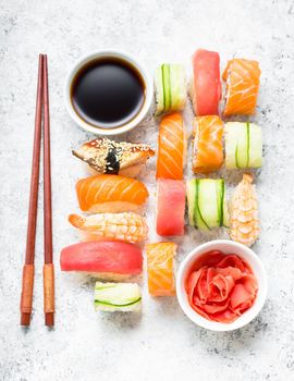 Assorted sushi set on white concrete background. Japanese sushi, rolls, soy sauce, ginger, chopsticks. Top view. Sushi nigiri. Japanese dinner/lunch. Different sushi mixed. Japanese food concept