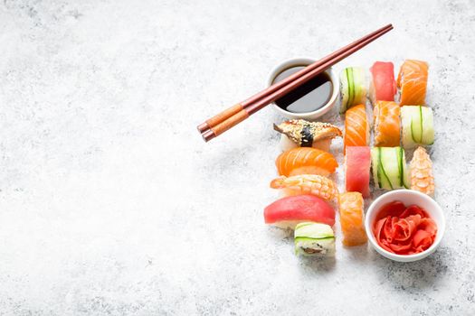 Assorted sushi set on white concrete background. Space for text. Japanese sushi, rolls, soy sauce, ginger, chopsticks. Top view. Sushi nigiri. Japanese dinner/lunch. Food frame. Different sushi mixed