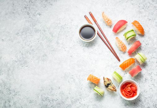 Assorted sushi set on white concrete background. Space for text. Japanese sushi, rolls, soy sauce, ginger, chopsticks. Top view. Sushi nigiri. Japanese dinner/lunch. Food frame. Different sushi mixed