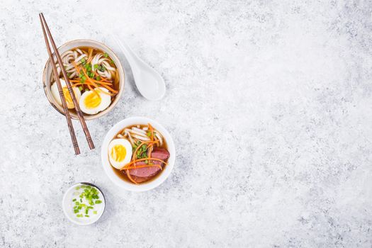 Bowls with Japanese soup ramen, chopsticks, white concrete rustic background. Traditional Asian soup with noodles, meat, eggs. Asian food. Japanese ramen for dinner. Space for text. Ramen, top view