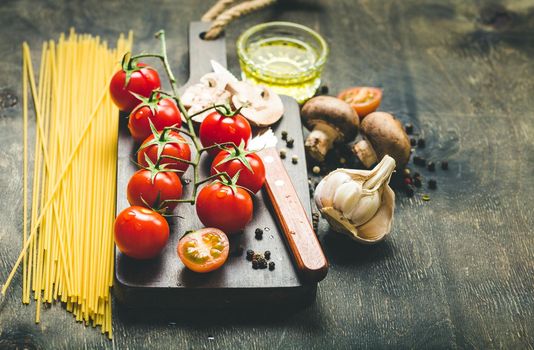 Cherry tomatoes, mushrooms, spaghetti, wooden cutting board, knife. Garlic, olive oil. Cooking concept. Space for text. Ingredients for cooking. Cooking dinner. Selective focus. Food preparing