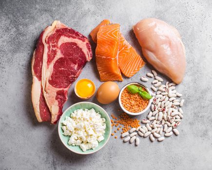 Assortment of natural sources of protein from food: meat, fish, chicken, dairy products, eggs, beans. Diet, healthy eating, wellness, bodybuilding concept, top view, stone background.