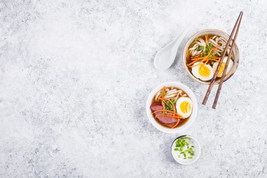Bowls with Japanese soup ramen, chopsticks, white concrete rustic background. Traditional Asian soup with noodles, meat, eggs. Asian food. Japanese ramen for dinner. Space for text. Ramen, top view