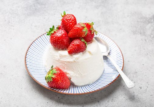 Fresh Italian cheese ricotta with strawberries on a plate with a spoon, grey rustic stone background, light summer dessert or snack, good for diet or healthy eating. Selective focus, close-up