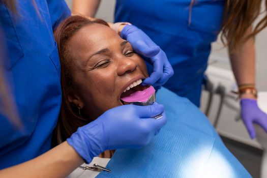 Close up of a female dentist's hands, placing an impression tray into one of her black female client's mouth, in order to take a sample denture at the dental clinic