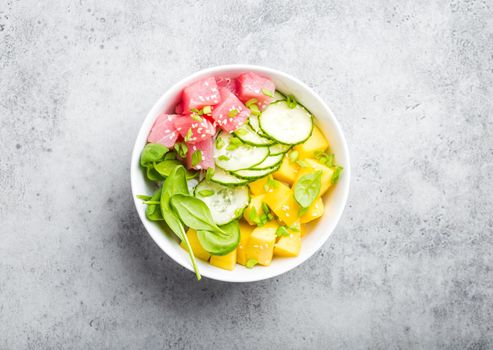 Top view of poke bowl with fresh raw tuna, mango, rice, spinach, cucumber. Traditional Hawaiian dish on rustic stone background. Healthy and clean eating concept. Poke with slices of raw fish