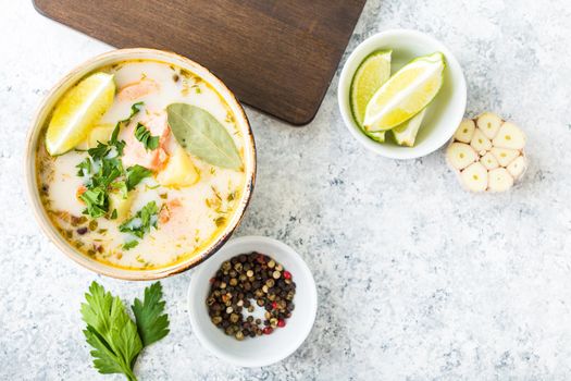 Salmon soup with potatoes, carrot, cream. Scandinavian/Norwegian fish soup in bowl, cutting board, spoon, rustic white concrete background. Space for text. Salmon soup for dinner. Top view. Close-up