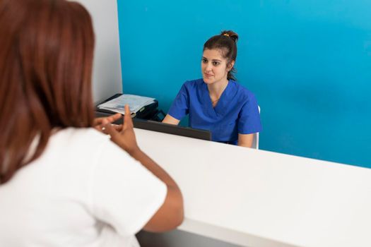 A female dentist talks to and greets one of her client sat the counter in the hall of the dental clinic