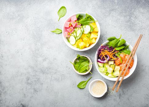 Two assorted poke bowls with raw fish and vegetables, space for text. Top view. Traditional Hawaiian dish, rustic stone background. Healthy clean eating concept. Poke with raw fish slices, copy space