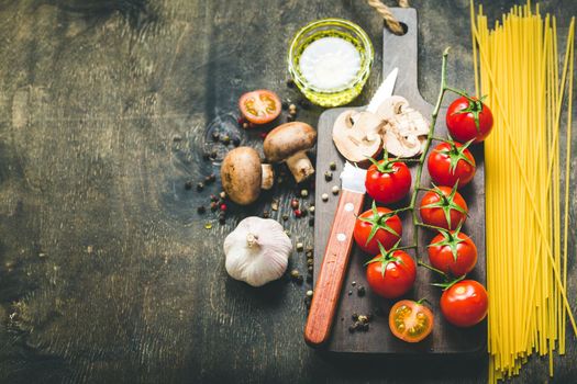 Cherry tomatoes, mushrooms, spaghetti, wooden cutting board, knife. Garlic, olive oil. Cooking background. Space for text. Ingredients for cooking. Cooking dinner. Selective focus. Food background