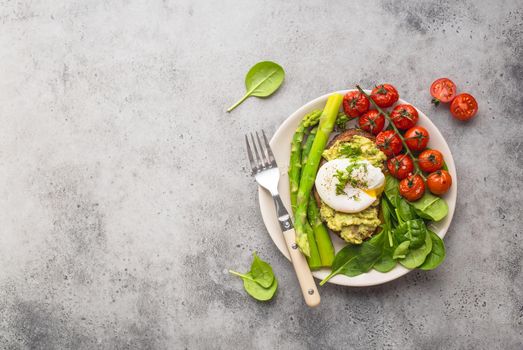 Healthy vegetarian meal plate. Toast, avocado, poached egg, asparagus, baked tomatoes, spinach. Stone background. Space for text. Vegetarian breakfast plate. Diet. Organic clean healthy food. Top view