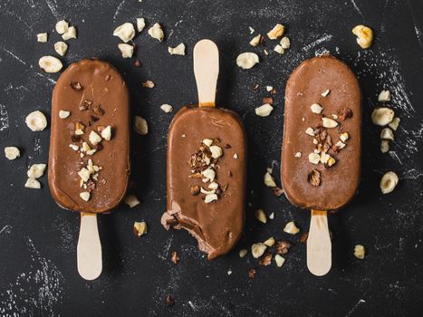 Milk chocolate popsicles with hazelnuts. Close-up. Ice cream popsicles covered with chocolate, sticks, black stone background. Top view. Chocolate ice cream bars, nuts. Dessert. Bitten popsicle