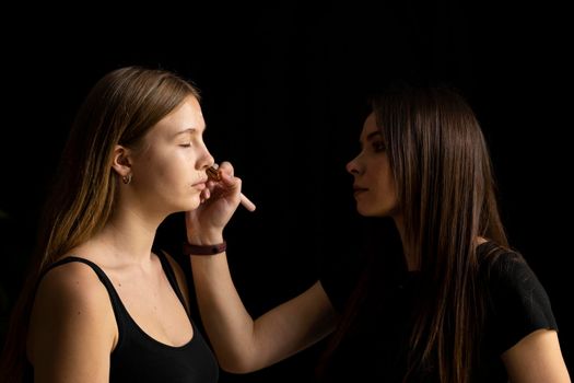 Makeup artist applying liquid tonal foundation on the face of the woman. Professional make up in a visage studio