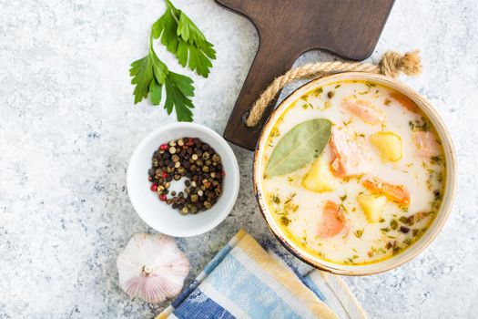 Salmon soup with potatoes, carrot, cream. Scandinavian/Norwegian fish soup in bowl, cutting board, spoon, rustic white concrete background. Space for text. Salmon soup for dinner. Top view. Close-up