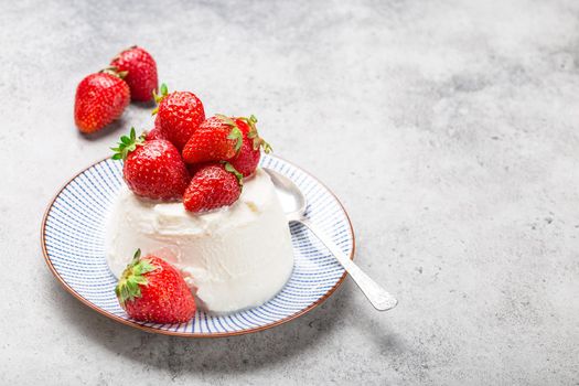 Close-up of fresh Italian cheese ricotta with strawberries on a plate with a spoon, grey rustic stone background, light summer dessert or snack, good for diet or healthy eating with space for text