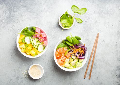 Two assorted poke bowls, raw tuna, salmon, vegetables, fruit. Top view. Traditional Hawaiian dish, rustic stone background. Healthy and clean eating concept. Poke with slices of raw fish, chopsticks