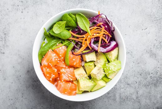 Top view of poke bowl with fresh raw salmon, avocado, rice, spinach, vegetables. Traditional Hawaiian dish on rustic stone background. Healthy and clean eating concept. Poke with slices of raw fish