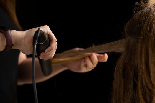 Hands of a hairdresser with a curling iron making a hairstyle for a curly girl in a professional beauty salon