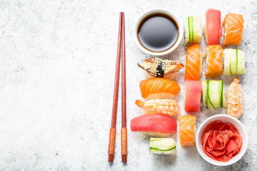 Assorted sushi set on white concrete background. Space for text. Japanese sushi, rolls, soy sauce, ginger, chopsticks. Top view. Sushi nigiri. Japanese dinner/lunch. Food frame. Different sushi mixed