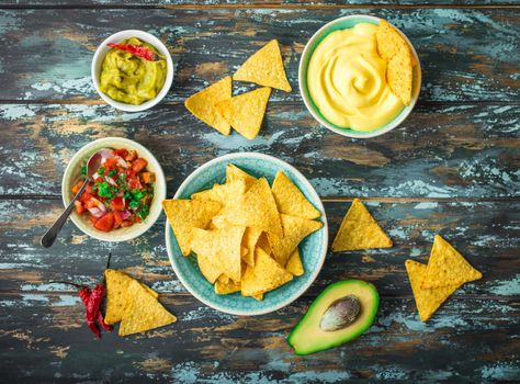 Mexican tortilla chips with guacamole, cheese, salsa dips. Nachos and assorted dips. Mexican party food, appetizers. Top view. Tortilla chips, sauces, hot pepper, avocado, rustic wooden background