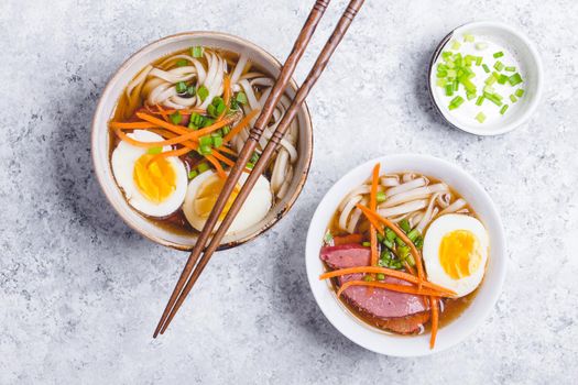 Bowls with Japanese soup ramen, chopsticks, white concrete rustic background. Traditional Asian soup with noodles, meat, broth, eggs. Asian food. Japanese ramen for dinner. Ramen, close-up. Overhead.