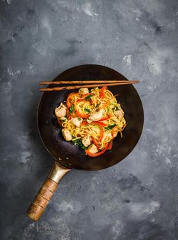 Stir fry noodles, traditional Chinese wok, chopsticks. Asian noodles with vegetables, chicken. Wok noodles, Chinese dinner/lunch. Rustic stone background. Top view. Asian/Chinese noodles. Stir frying.