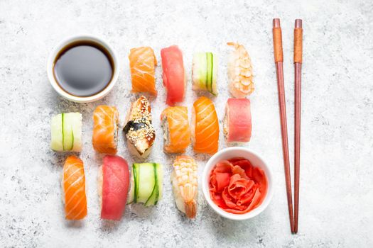 Assorted sushi set on white concrete background. Japanese sushi, rolls, soy sauce, ginger, chopsticks. Top view. Sushi nigiri. Japanese dinner/lunch. Different sushi mixed. Japanese food concept