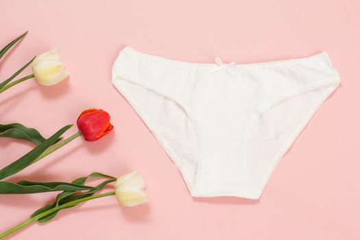 White cotton panties with tulip flowers on a pink background. Woman underwear set. Top view.