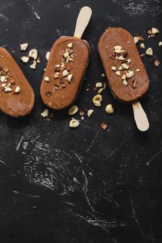 Milk chocolate popsicles with hazelnuts. Close-up. Ice cream popsicles covered with chocolate, sticks, black stone marble background. Space for text. Top view. Chocolate ice cream bars, nuts. Dessert