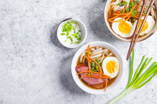 Bowls with Japanese soup ramen, chopsticks, white concrete rustic background. Traditional Asian soup with noodles, meat, eggs. Asian food. Japanese ramen for dinner. Ramen, close-up. Space for text.