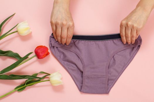 Woman is holding a brown cotton panties with tulip flowers on a pink background. Woman underwear set. Top view.