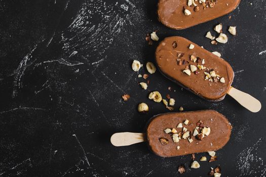 Milk chocolate popsicles with hazelnuts. Close-up. Ice cream popsicles covered with chocolate, sticks, black stone marble background. Space for text. Top view. Chocolate ice cream bars, nuts. Dessert