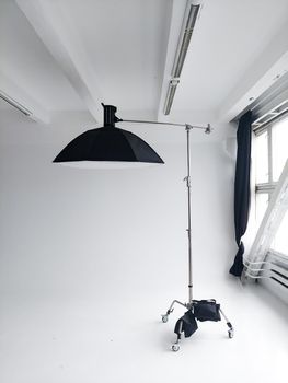 Professional photo flash light with a big softbox on a c-stand on a cyclorama in modern photo studio with a huge windows. Professional lighting equipment, flashes, c-stands