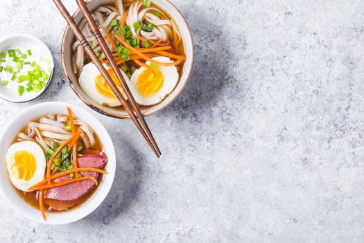 Bowls with Japanese soup ramen, chopsticks, white concrete rustic background. Traditional Asian soup with noodles, meat, eggs. Asian food. Japanese ramen for dinner. Ramen, close-up. Space for text.