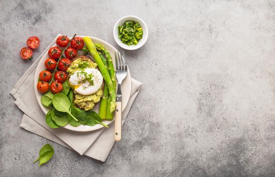Healthy vegetarian meal plate. Toast, avocado, poached egg, asparagus, baked tomatoes, spinach. Stone background. Space for text. Vegetarian breakfast plate. Diet. Organic clean healthy food. Top view