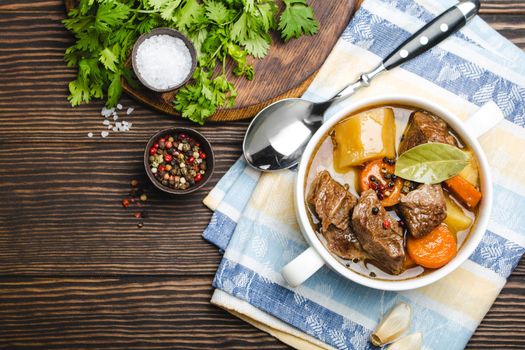 Close-up of slow cooked meat stew ragout in bowl with beef, potato, carrot, broth on wooden rustic background, top view with space for text. Hot homemade food for dinner, meat casserole copy space.