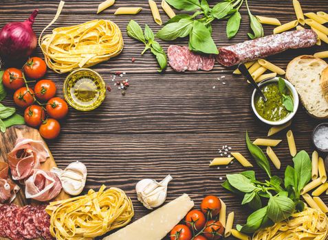 Top view of Italian traditional food, appetizers and snacks as salami, prosciutto, cheese, pesto, ciabatta, olive oil, pasta on rustic wooden background with space for text in centre, retro style