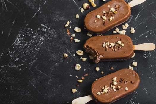 Milk chocolate popsicles with hazelnuts. Close-up. Ice cream popsicles covered with chocolate, sticks, black stone marble background. Space for text. Top view. Chocolate ice cream bars, nuts. Dessert