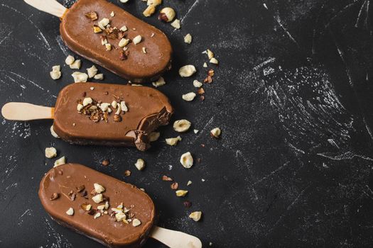 Milk chocolate popsicles with hazelnuts. Close-up. Ice cream popsicles covered with chocolate, sticks, black stone marble background. Space for text. Top view. Chocolate ice cream bars, nuts. Dessert