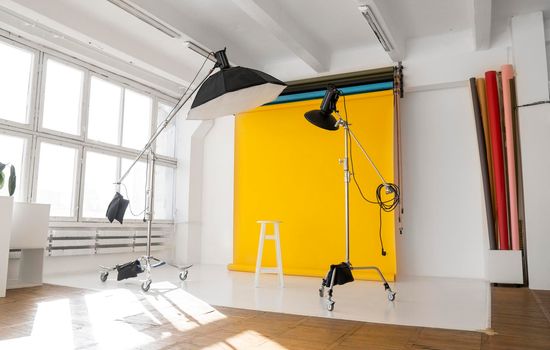 Yellow background roll with a white chair and two professional flash on a c-stands. Sunny daylight photo studio interior with set of professional equipment