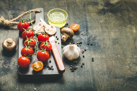 Cherry tomatoes, mushrooms on wooden cutting board, knife. With garlic, olive oil. Cooking background. Space for text. Raw ingredients for cooking. Cooking dinner. Selective focus. Food background