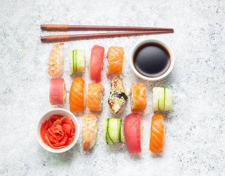 Assorted sushi set on white concrete background. Japanese sushi, rolls, soy sauce, ginger, chopsticks. Top view. Sushi nigiri. Japanese dinner/lunch. Different sushi mixed. Japanese food concept