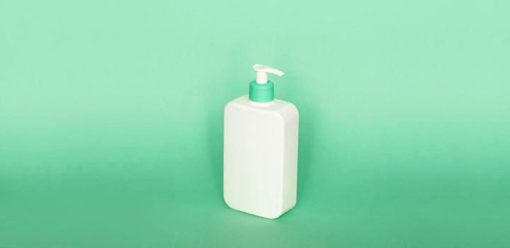 White plastic soap dispenser pump bottle isolated on green background. Skin care lotion. Bathing essential product. Shampoo bottle. Bath and body lotion. Fine liquid hand wash. Bathroom accessories