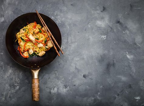 Stir fry noodles in traditional Chinese wok, chopsticks, ingredients. Space for text. Asian noodles with vegetables, chicken. Wok noodles. Rustic stone background. Top view. Asian/Chinese dinner