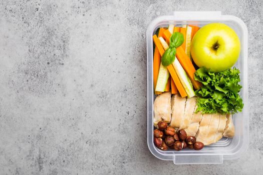 Healthy food lunchbox for office or school: chicken fillet, carrot, cucumber sticks, salad, apple. Preparation and packaging of meal to support balanced lifestyle or diet, stone background, copy space