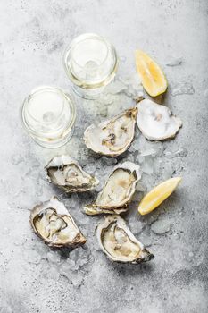 Close-up of half dozen of fresh opened oysters and shells with lemon wedges, two glasses of white wine or champagne, top view, grey rustic concrete background. Romantic or celebration with oysters.